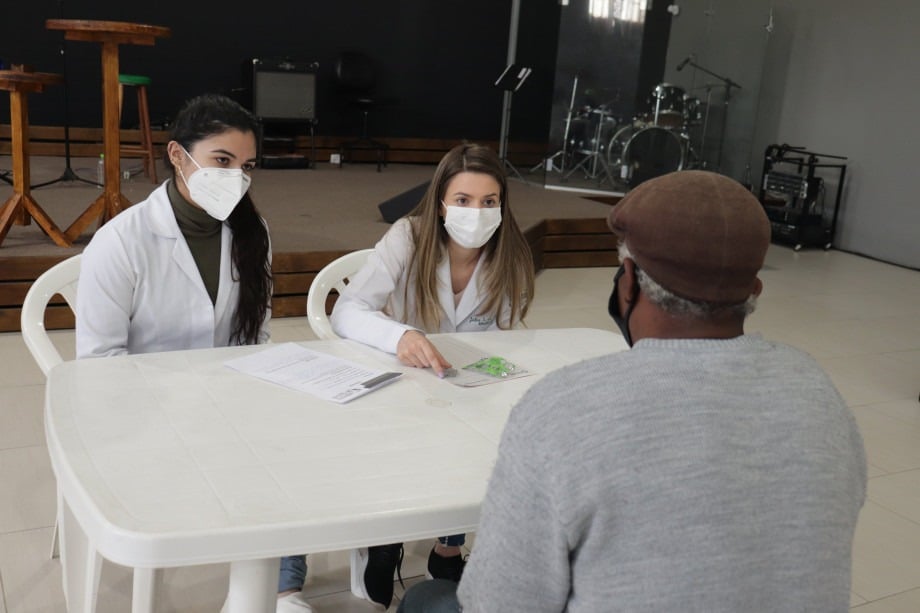 Duas estudantes da Medicina da UCPel de jaleco e máscara atendem um paciente